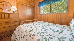 Une pièce en bois avec un lit, une commode, un miroir et une fenêtre avec des stores.