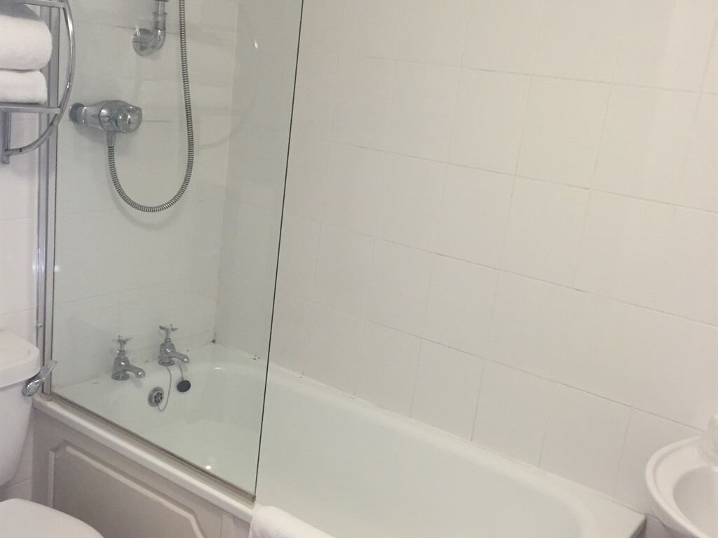 Ett badrum med en dusch som är avskärmad med glasväggar, ett vitt badkar och en vit handfat.