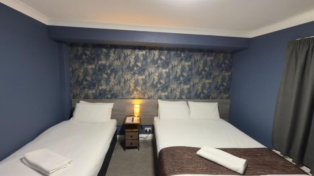Ein Hotelzimmer mit zwei Einzelbetten, einem Nachttisch mit Lampe und einem gemusterten Kopfteil.