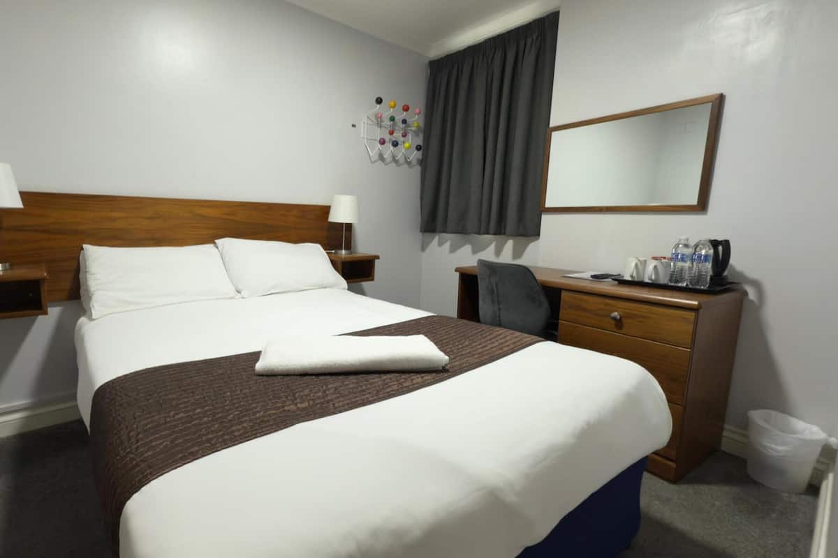 Ein Hotelzimmer mit einem großen Bett, zwei Nachttischen inklusive Lampen, einem Schreibtisch mit Stuhl, einem Spiegel und einer Wanddekoration.