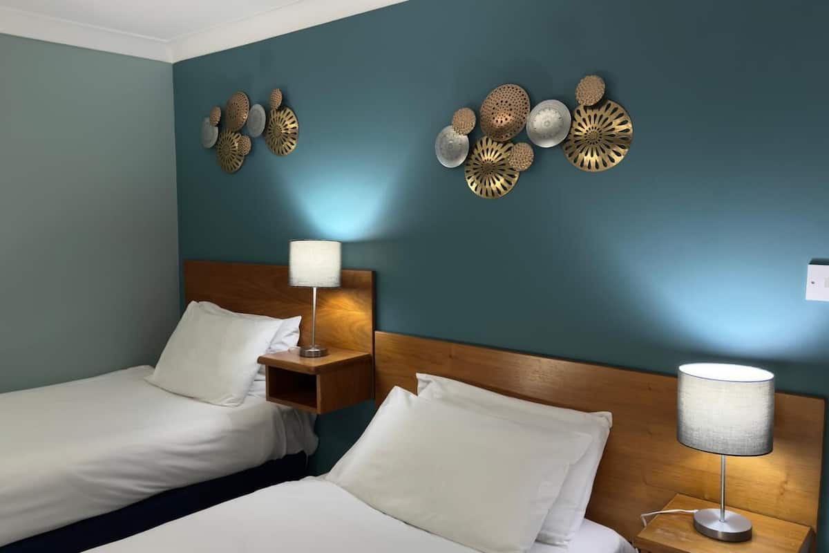 Ein Hotelzimmer mit zwei Einzelbetten, Holz-Kopfteilen und Wandleuchten.