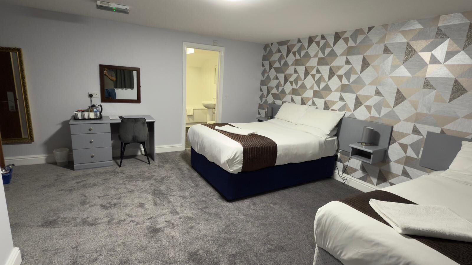 A bedroom with a bed, a desk, a chair, a dresser, and a bathroom visible through an open door.