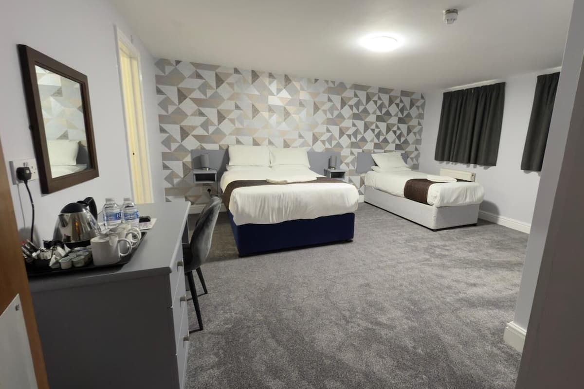 Ein Hotelzimmer mit Bett, Schreibtisch und Stuhl. Auf dem Schreibtisch steht ein Tablett mit Tassen und einem Wasserkocher.