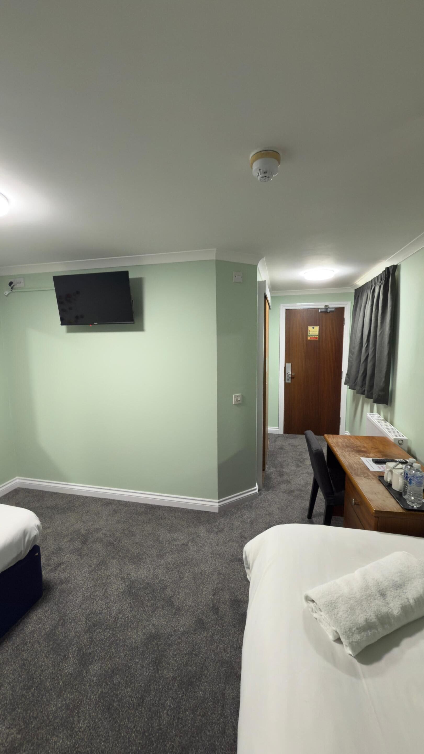 A hotel room with two beds, a desk with a chair, a television mounted on the wall, and a door leading to another room.