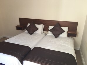 Two single beds with dark brown headboards and throw blankets, accompanied by a nightstand.
