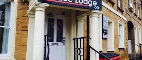 The Terrace Lodge Hotel facade with a stone exterior, a white door, and a red waste bin.