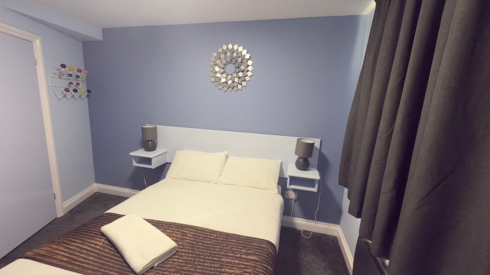 A hotel room with a bed, two bedside tables, a wall decoration, and a curtain.