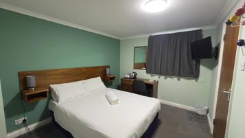 A hotel room with a bed, bedside table, lamp, and a TV mounted on the wall.