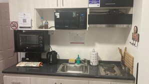 A compact kitchen with a microwave, kettle, and sink. There are cabinets, a sign indicating WiFi availability, and a QR code.