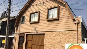 Ein zweistöckiges Gebäude mit einer braunen Holzfassade, einer Garagentür und einem kleinen Fenster im oberen Geschoss.