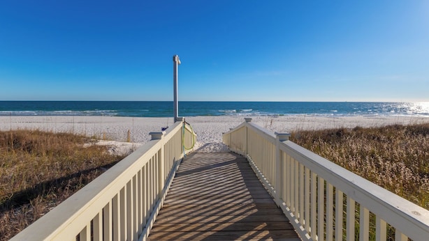 Une promenade en bois qui mène à une plage, avec un ciel bleu dégagé.