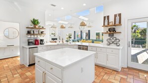 Une cuisine spacieuse avec des meubles blancs, un grand îlot central et une vue sur l’extérieur.