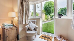 Una habitación acogedora con una silla, una lámpara, una ventana con cortinas y vistas a un jardín.