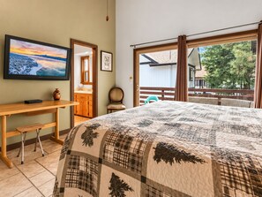 A bedroom with a large bed, a wooden desk, a television, and a view of the outdoors.