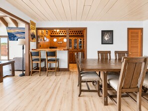 A dining area with a wooden table and chairs, a kitchen with wooden cabinets, and a view of the outdoors.