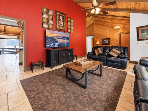 A living room with a red wall, a ceiling fan, a fireplace, and a large window.