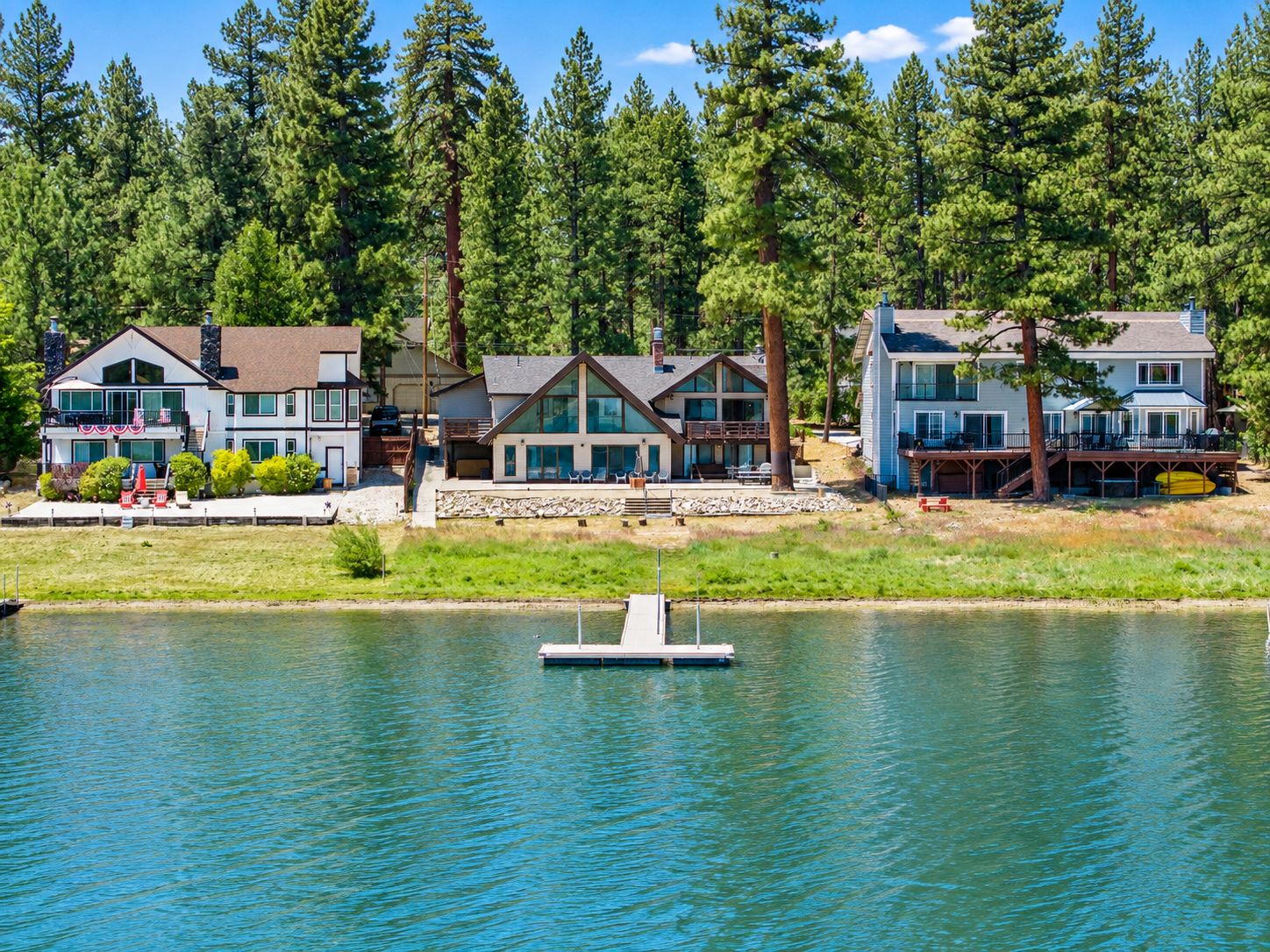 A lakeside property with multiple houses, a dock, and a forest backdrop.