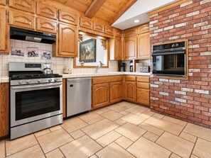 A kitchen with wooden cabinets, a brick wall, stainless steel appliances, and a tiled floor.