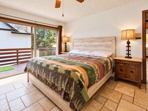 A bedroom with a large bed, two bedside lamps, a wooden headboard, and a view through a sliding glass door to an outdoor deck.