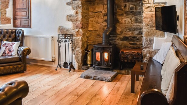 Una sala de estar acogedora con chimenea de piedra, sofá de cuero y televisor montado en la pared.