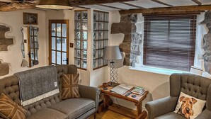 Una sala de estar acogedora con un sofá, un sillón y una mesa de centro. Hay libros, una lámpara y un marco de fotos sobre la mesa.