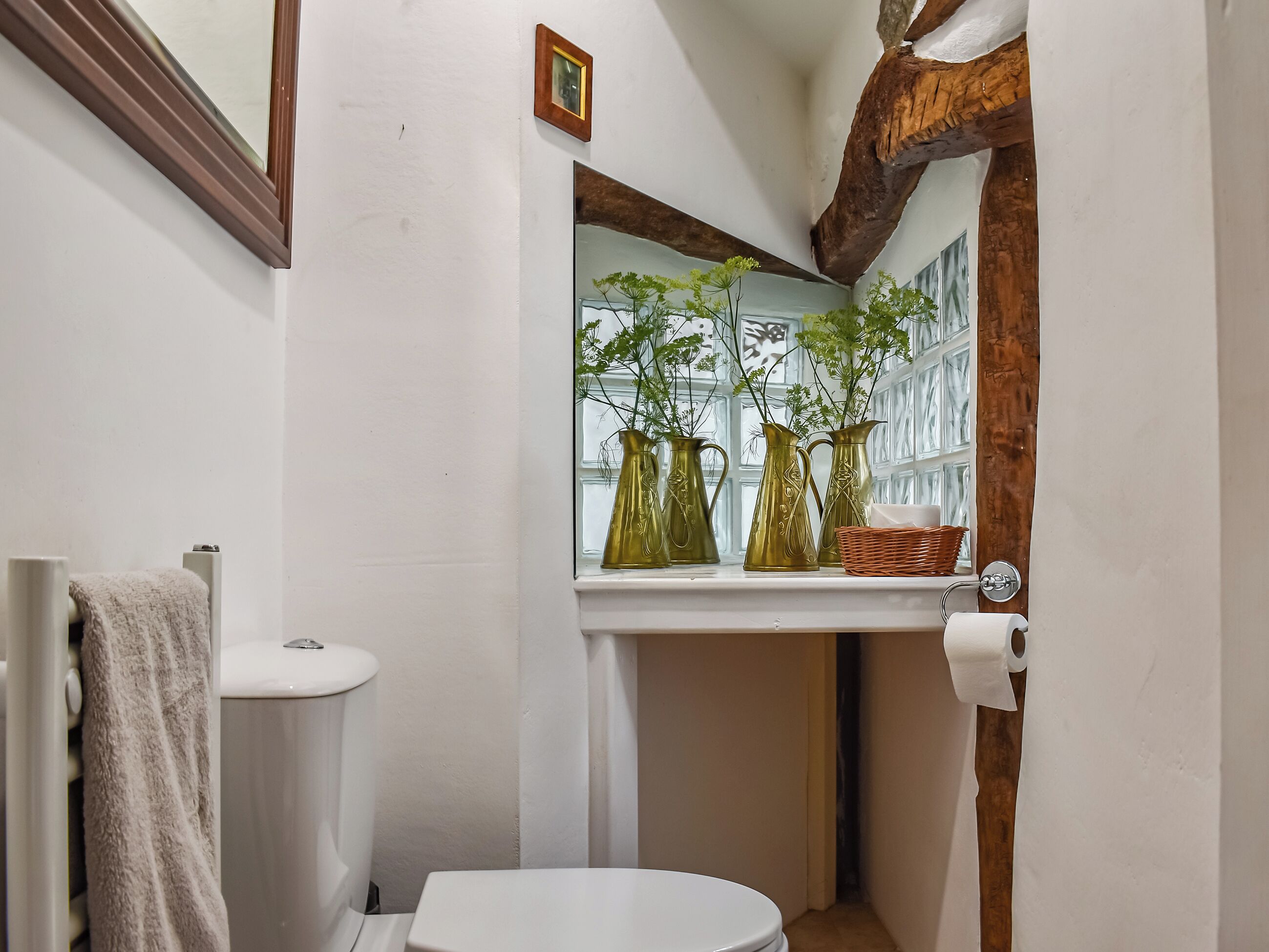 A bathroom with a white toilet, a towel rack, and a window with decorative vases and a wicker basket.