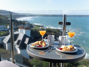 A table with breakfast items and drinks, overlooking a scenic view of the ocean and a coastal town.