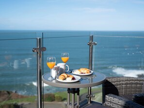 A table with breakfast items and a glass of orange juice, overlooking the ocean.