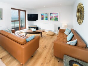 A modern living room with leather sofas, a flat-screen TV, artwork, and a view through a large window.