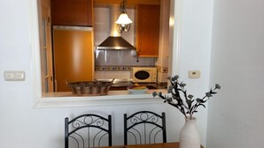 Un comedor con una mesa, sillas, un florero con flores secas y vistas a una cocina con armarios de madera, una estufa y un microondas.