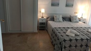 Un dormitorio con cama, dos mesitas de noche, una mesita auxiliar, una lámpara de pared y una puerta.