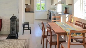 A cozy kitchen with a dining area, featuring a wooden table and chairs, a radiator, and a window with a view of greenery. - Nice apartment in Simrishamn with WiFi (Simrishamn)