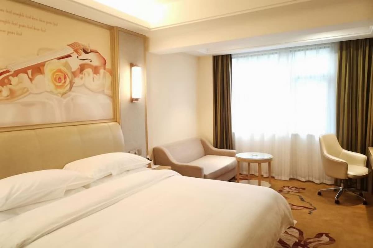 A hotel room with a large bed, two armchairs, a small round table, and a large window with curtains.