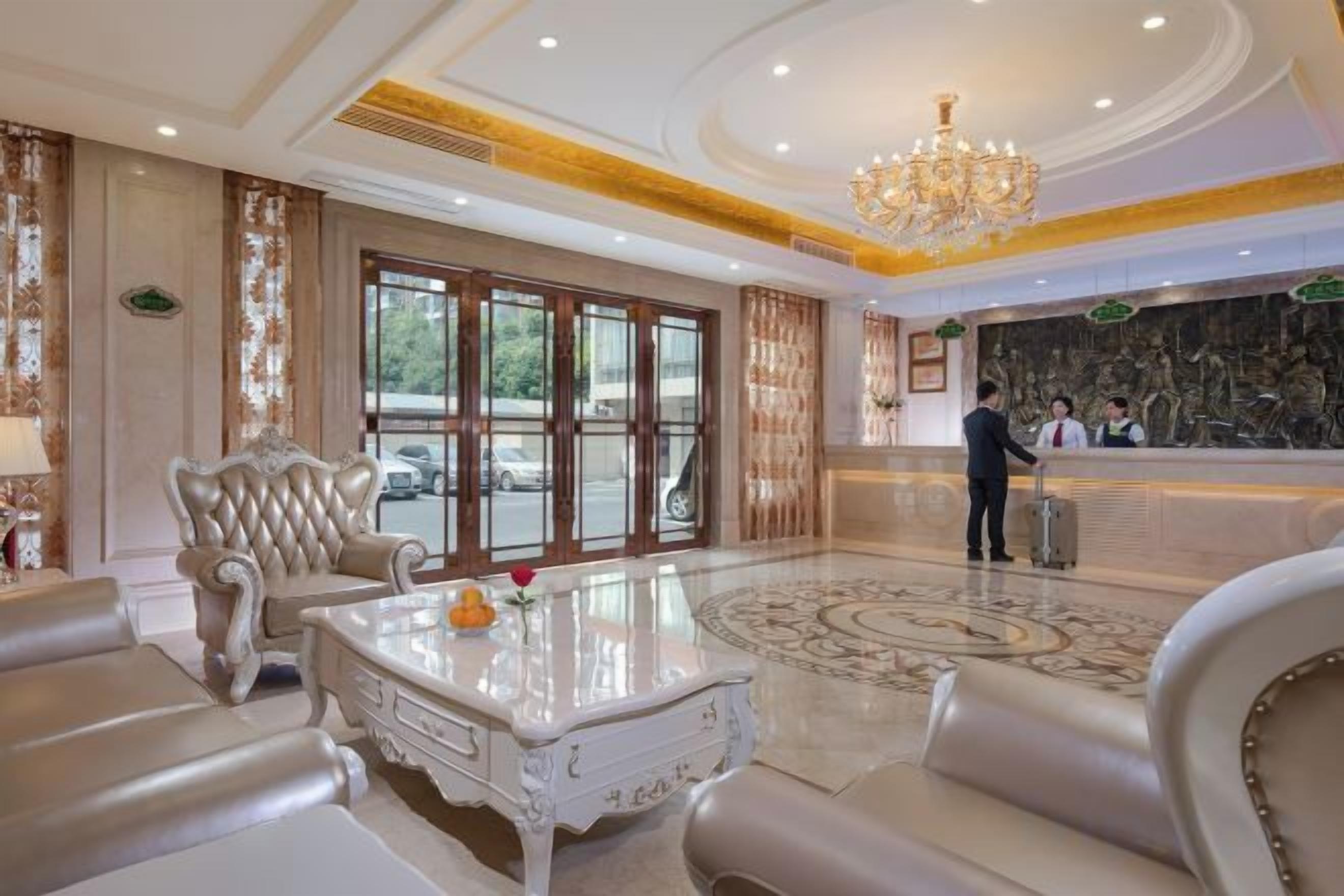 A spacious lobby with a grand chandelier, a reception desk, and a large window.