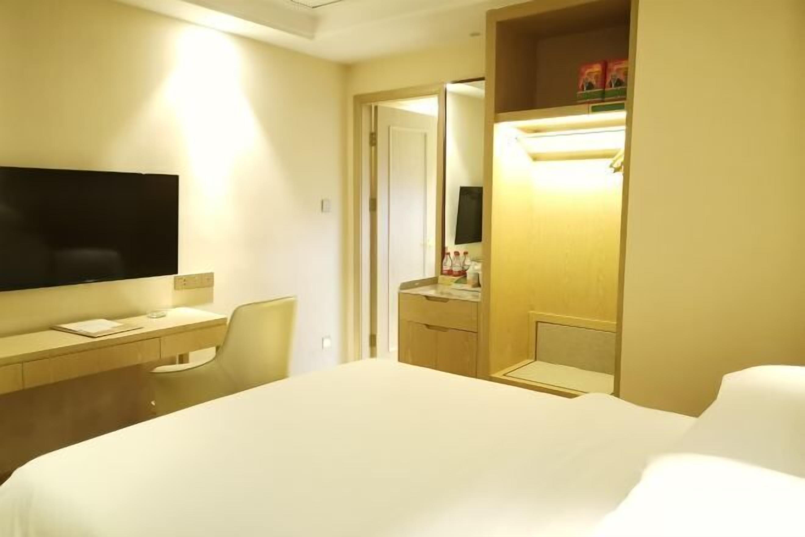 Habitación de hotel con cama, escritorio, televisor de pantalla plana, silla, armario y espejo.
