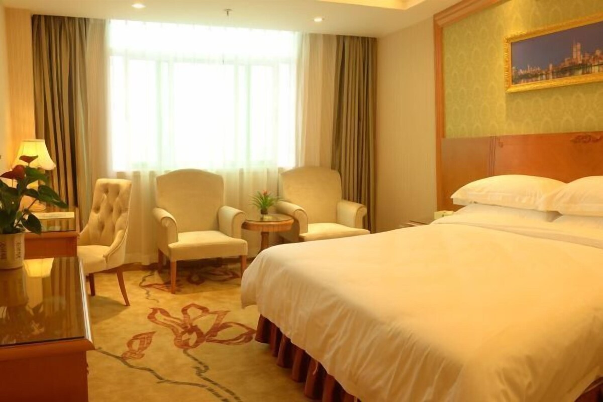 A hotel room with a large bed, two armchairs, a small table, and a lamp.