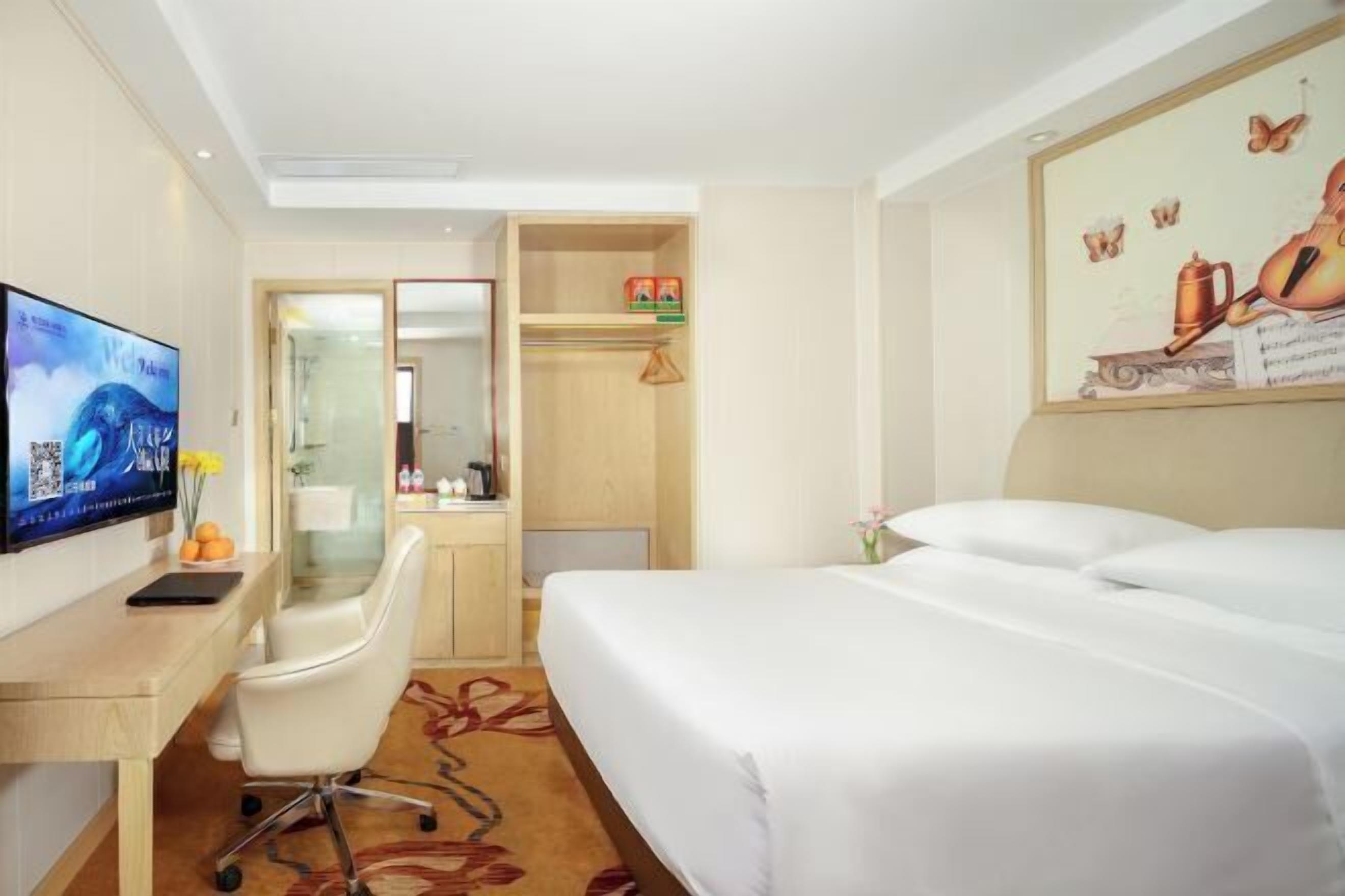 Ein Hotelzimmer mit einem Bett, einem Schreibtisch mit Computer, einem Sessel, einem Kleiderschrank und einem Fernseher.