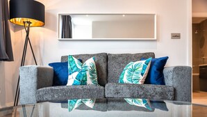 A grey sofa with blue and green patterned cushions, a black floor lamp, and a large mirror on the wall.