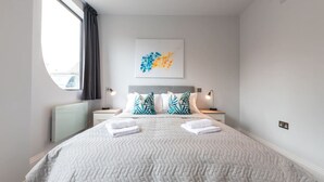 A modern bedroom with a large bed, two nightstands, a radiator, and a window with curtains.