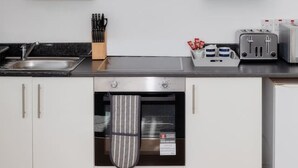 Una cocina moderna con armarios blancos, una campana extractora de acero inoxidable, un horno empotrado y una encimera con un tostador y cuchillos.