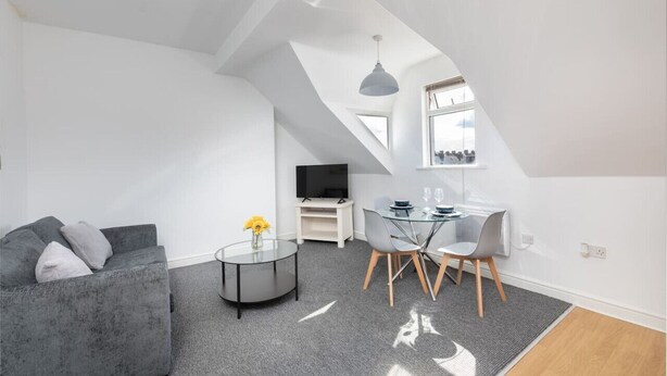 Una sala moderna con un sofá gris, una mesa de centro de vidrio y un comedor con una mesa y sillas de vidrio.