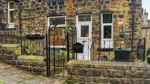 A stone building with a black iron gate, a white door, and a window with a hanging plant.