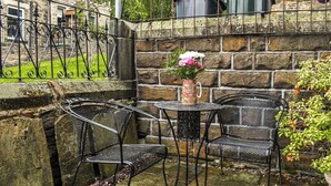 A stone wall with metal chairs and a table, a flower vase, and a building in the background.