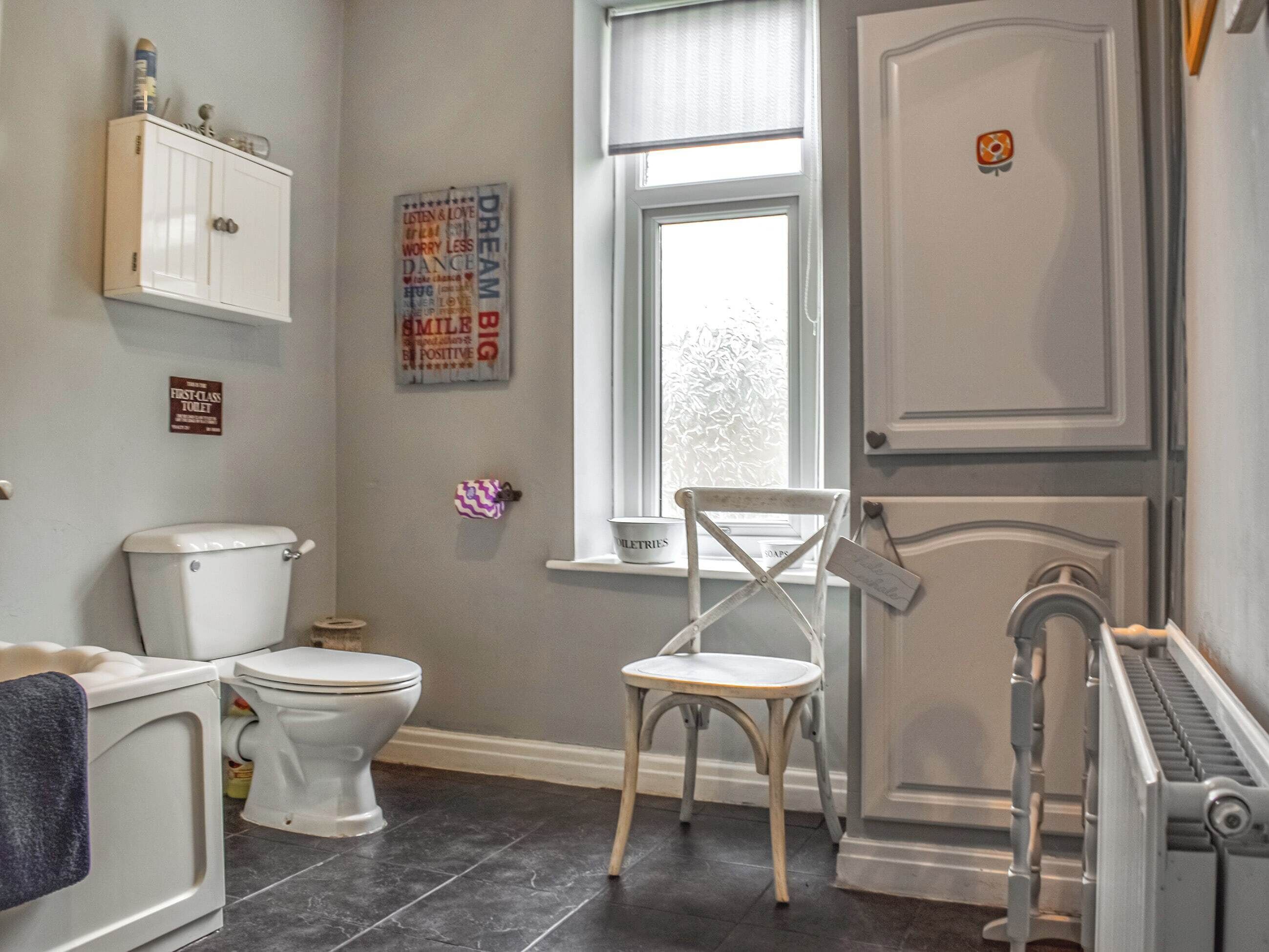 Een badkamer met toilet, stoel, radiator en raam.