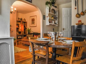 A cozy dining area with a wooden table set for four, surrounded by wooden chairs. A chandelier hangs above, and a bookshelf filled with various items is visible in the background. - 2 bedroom accommodation in Haworth (Haworth)