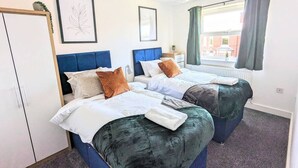 Una habitación de hotel con dos camas, un armario, una ventana con cortinas y cuadros en las paredes.