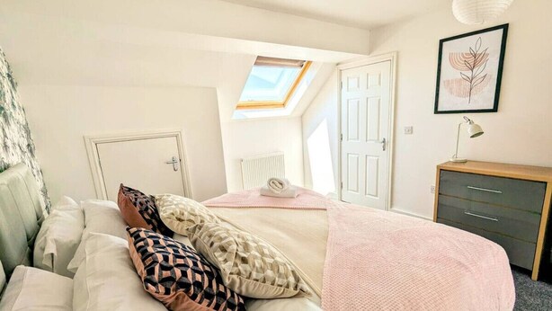 Un dormitorio con cama, escritorio, silla, radiador, puerta y tragaluz.