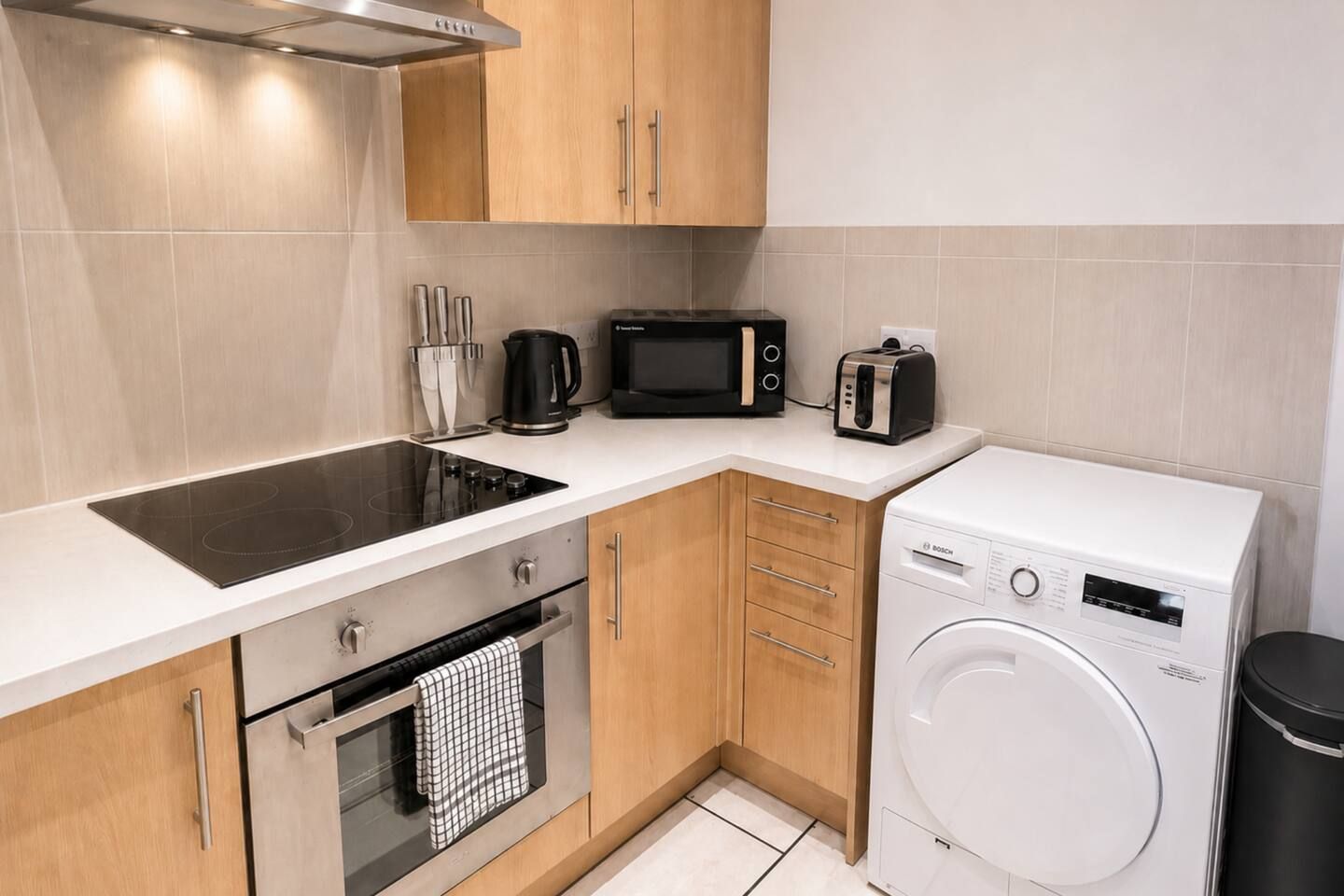 A compact kitchen with a built-in stovetop, a microwave, a toaster, and a front-loading washing machine.
