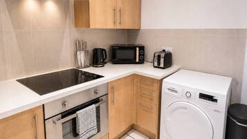 A compact kitchen with a built-in stovetop, a microwave, a toaster, and a front-loading washing machine.
