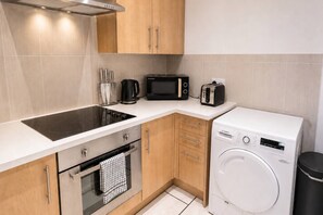 Una cucina compatta con piano cottura integrato, forno a microonde, tostapane e lavatrice a carica frontale.